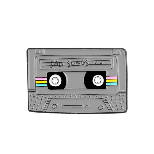 Enamel Pin shaped like a cassette tape that has "Sad Songs" written on the label.