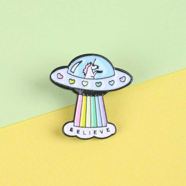 Front view of the Unicorn in a flying saucer enamel pin with the word "Believe" at the bottom.